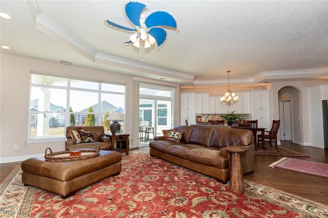 living area with a wealth of natural light, crown molding, a raised ceiling, and wood finished floors