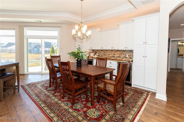 dining space featuring a tray ceiling, arched walkways, ornamental molding, a notable chandelier, and light wood-type flooring