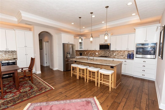 kitchen with a breakfast bar, a sink, arched walkways, appliances with stainless steel finishes, and a raised ceiling