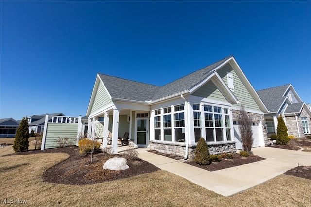 rear view of property featuring driveway, an attached garage, roof with shingles, and a sunroom