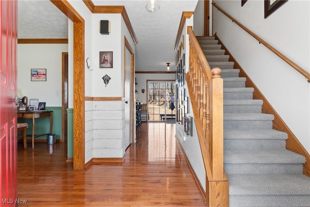 foyer entrance with a wainscoted wall, wood finished floors, crown molding, and stairway