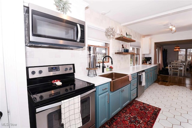 kitchen featuring blue cabinetry, a sink, light countertops, appliances with stainless steel finishes, and backsplash