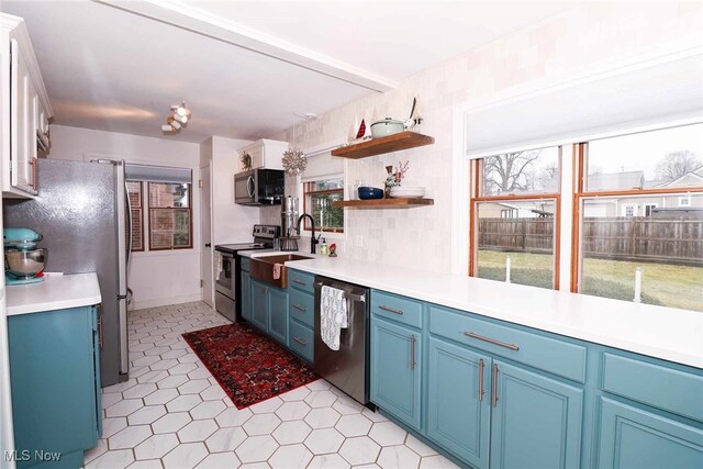 kitchen with blue cabinets, stainless steel appliances, light countertops, and a sink