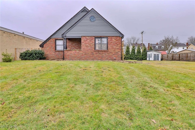 rear view of house featuring a storage unit, brick siding, a lawn, and fence