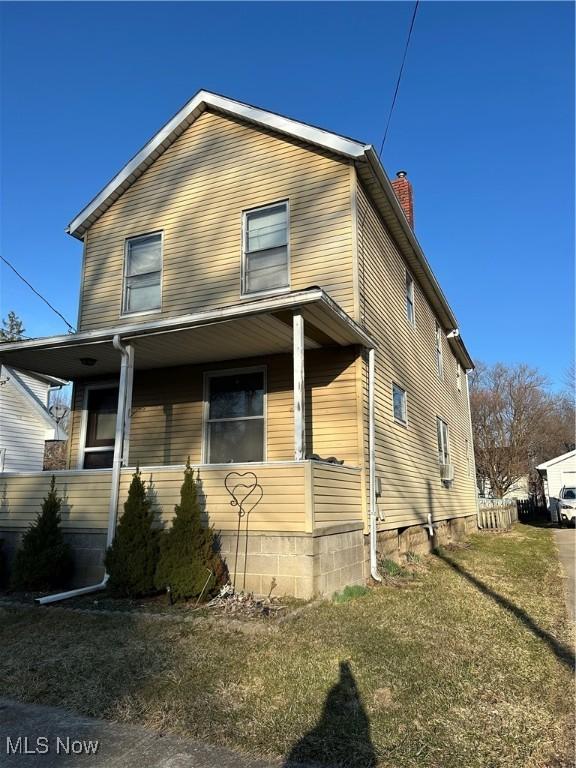 view of front of property featuring a front yard, covered porch, and a chimney