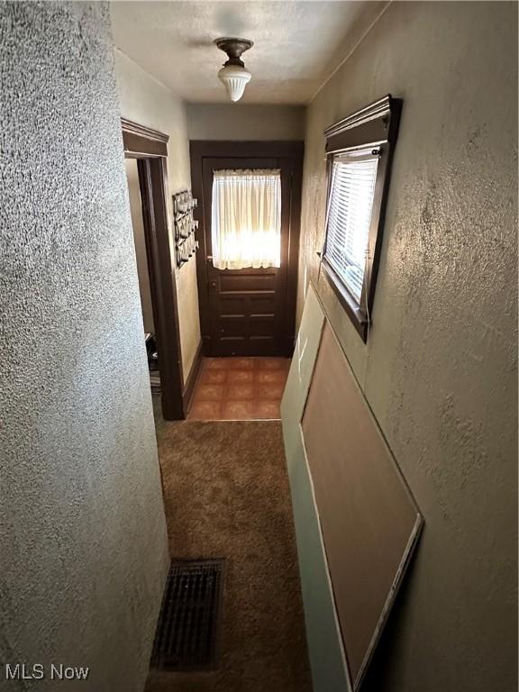 corridor with visible vents, carpet floors, a textured ceiling, and a textured wall