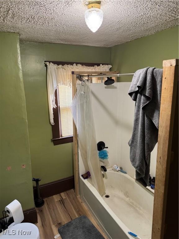 full bathroom featuring toilet, shower / bath combo, a textured ceiling, wood finished floors, and baseboards