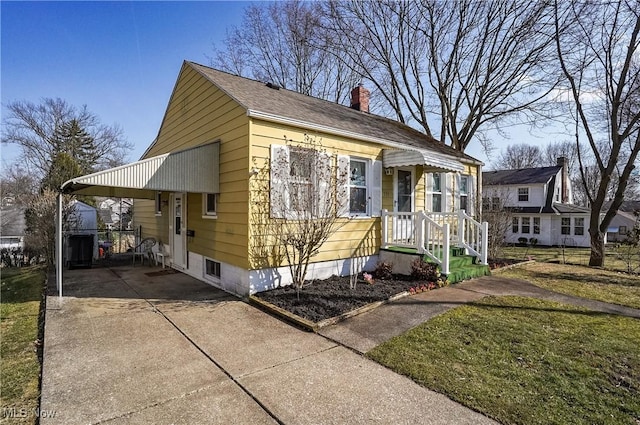 view of front of property with an attached carport, concrete driveway, a chimney, and a front lawn