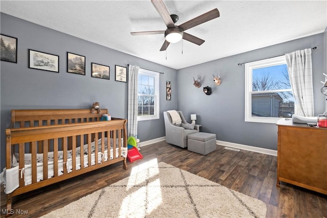 bedroom with ceiling fan, baseboards, a crib, and wood finished floors