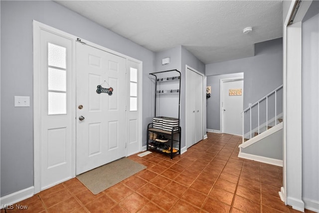 foyer entrance with tile patterned floors, stairway, baseboards, and a textured ceiling