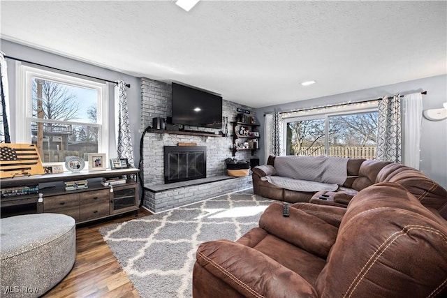 living room with a brick fireplace, wood finished floors, a wealth of natural light, and a textured ceiling