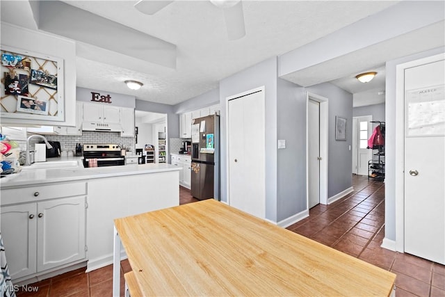 kitchen featuring tasteful backsplash, under cabinet range hood, appliances with stainless steel finishes, a peninsula, and a textured ceiling