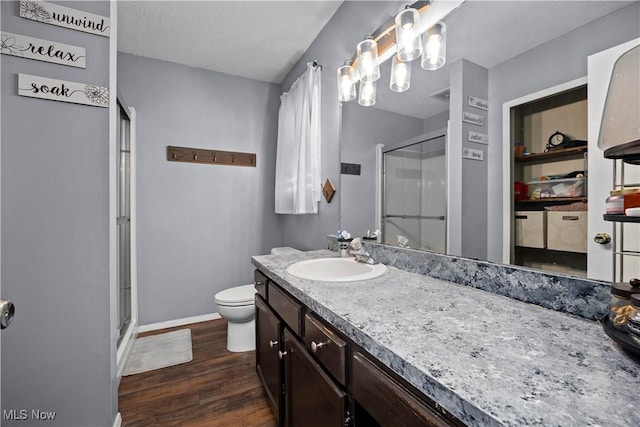 bathroom featuring toilet, wood finished floors, a shower stall, baseboards, and vanity