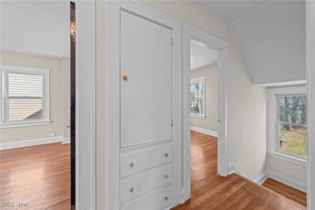 hallway featuring baseboards, wood finished floors, and vaulted ceiling