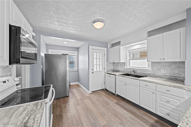 kitchen featuring a healthy amount of sunlight, wood finished floors, a sink, stainless steel appliances, and white cabinetry