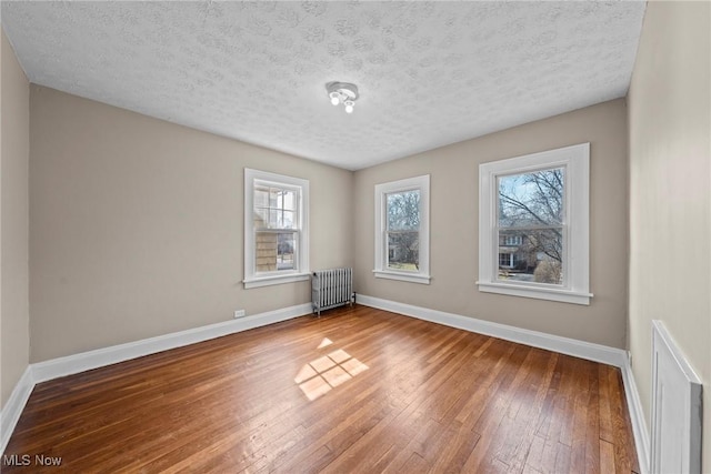 unfurnished room featuring radiator, a textured ceiling, baseboards, and hardwood / wood-style floors