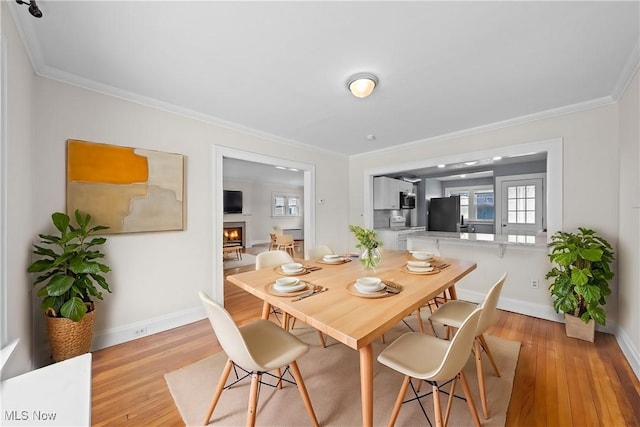 dining area with light wood finished floors, baseboards, crown molding, and a lit fireplace