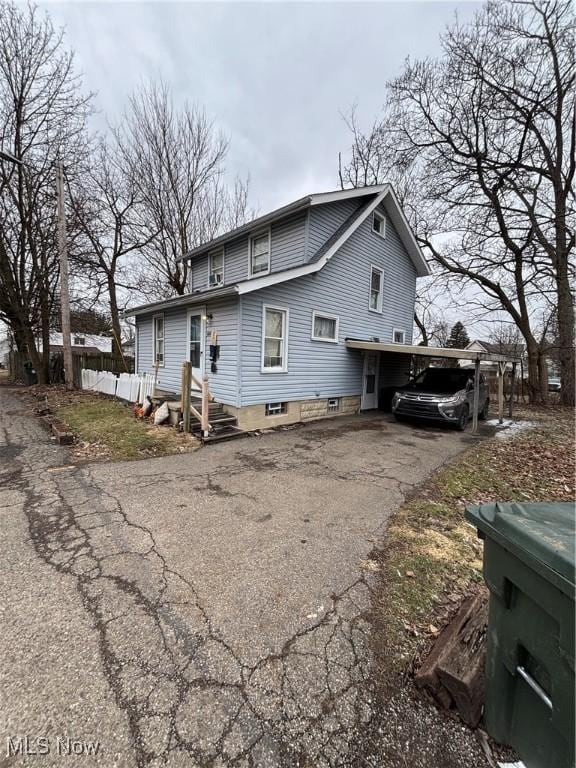 rear view of property with aphalt driveway, a carport, and fence