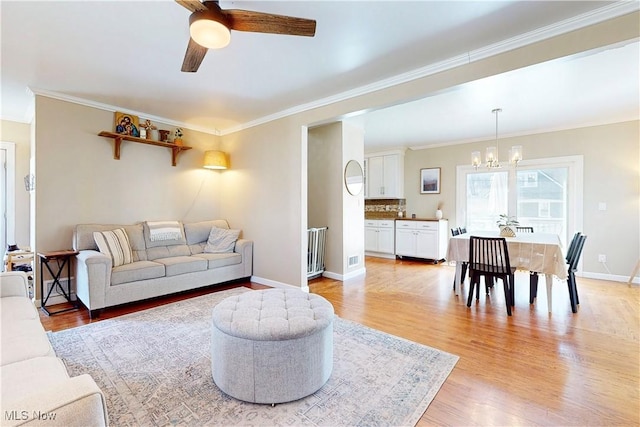 living area with light wood finished floors, ceiling fan with notable chandelier, crown molding, and baseboards