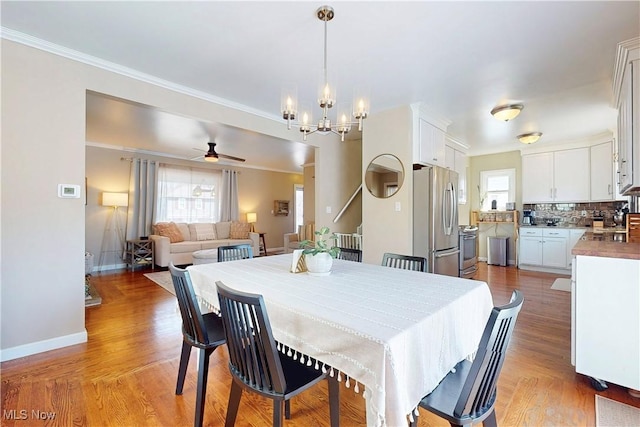 dining room featuring baseboards, ceiling fan with notable chandelier, crown molding, and light wood finished floors