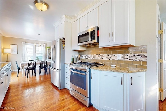 kitchen featuring decorative light fixtures, backsplash, appliances with stainless steel finishes, white cabinets, and light wood finished floors