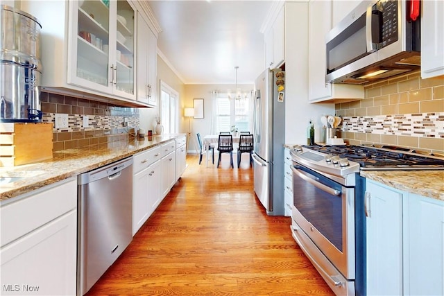 kitchen featuring tasteful backsplash, glass insert cabinets, light wood-style flooring, stainless steel appliances, and white cabinetry