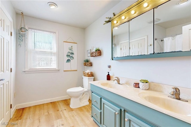 bathroom with double vanity, toilet, wood finished floors, and a sink