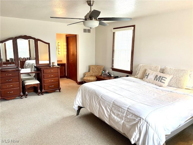 bedroom featuring connected bathroom, light colored carpet, visible vents, and ceiling fan