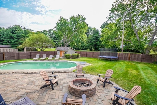 view of swimming pool featuring a trampoline, an outdoor fire pit, a lawn, a fenced backyard, and a patio area