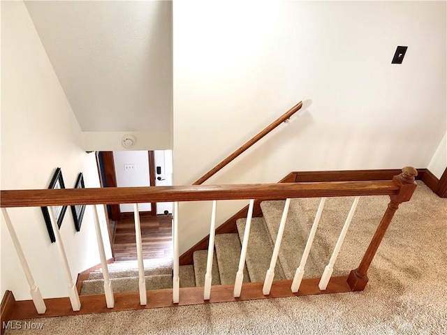 staircase featuring lofted ceiling, carpet, and baseboards