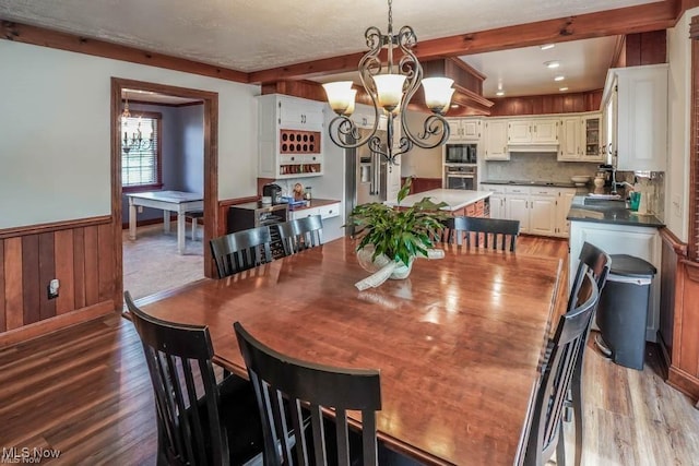 dining room featuring beam ceiling, a notable chandelier, wood finished floors, and wainscoting