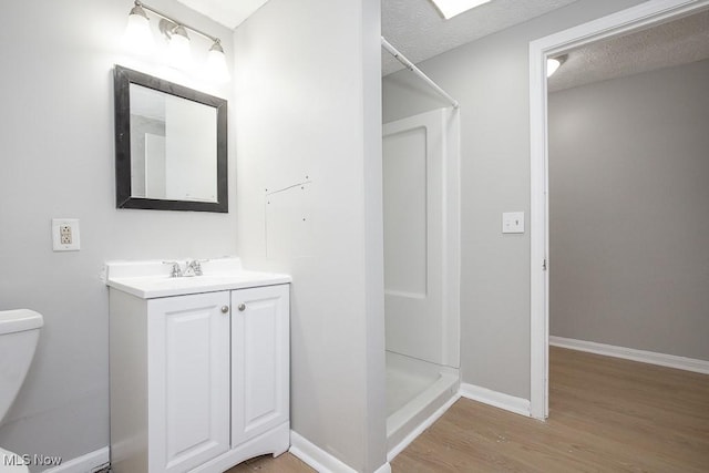 bathroom with vanity, wood finished floors, a stall shower, a textured ceiling, and toilet