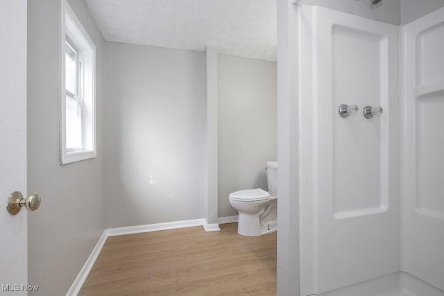 bathroom with walk in shower, baseboards, toilet, wood finished floors, and a textured ceiling