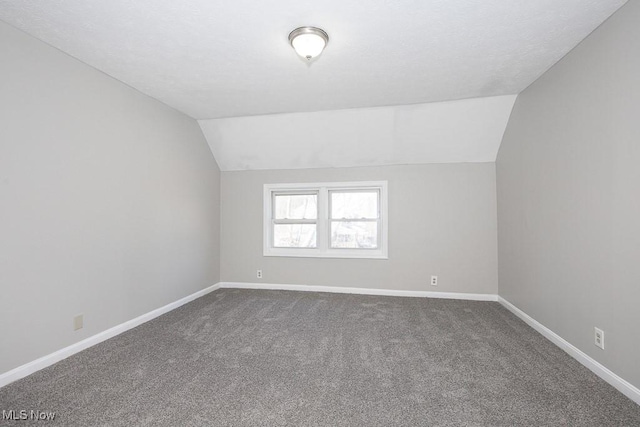 additional living space featuring baseboards, lofted ceiling, and dark carpet