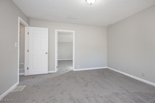 unfurnished bedroom featuring baseboards, visible vents, carpet floors, a spacious closet, and a textured ceiling