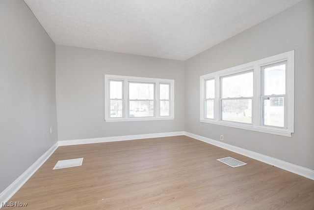 empty room with baseboards, visible vents, light wood finished floors, and a textured ceiling