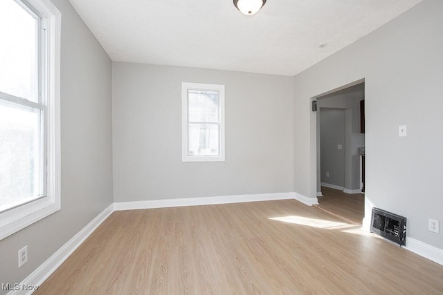 unfurnished room featuring light wood-type flooring, baseboards, a healthy amount of sunlight, and heating unit