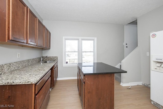 kitchen with a textured ceiling, white fridge with ice dispenser, light wood-type flooring, and a sink