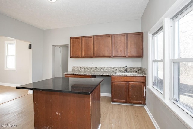 kitchen with a textured ceiling, light wood-style floors, baseboards, and a sink