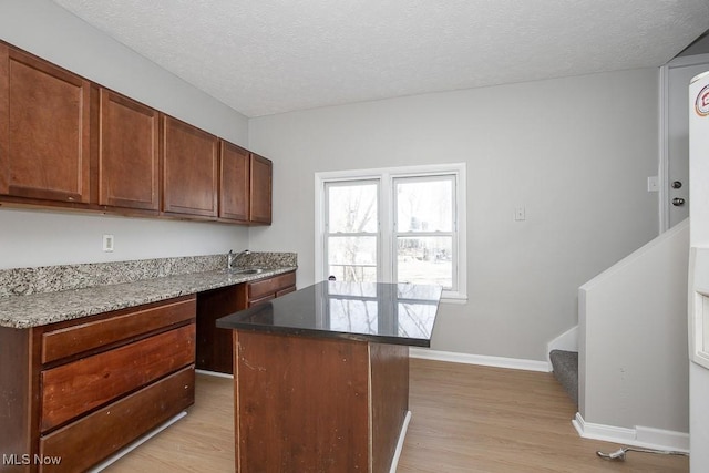 kitchen with baseboards, a textured ceiling, a center island, and light wood finished floors