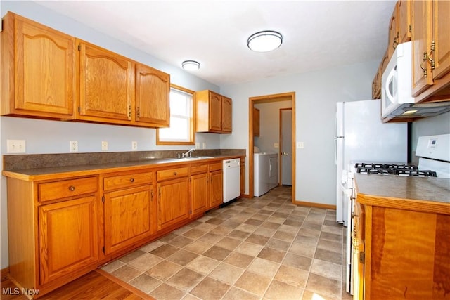 kitchen with a sink, white appliances, brown cabinets, and washer and clothes dryer