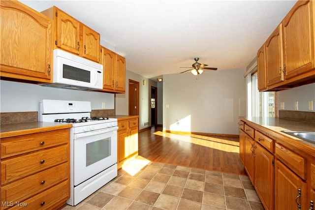 kitchen with white appliances, brown cabinetry, baseboards, ceiling fan, and light wood-style floors