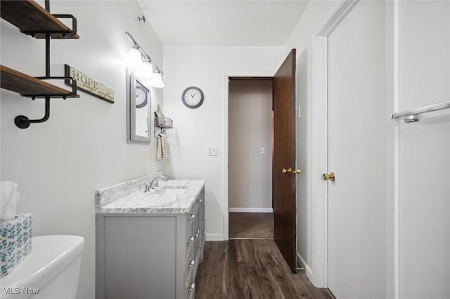 half bathroom with baseboards, toilet, wood finished floors, and vanity