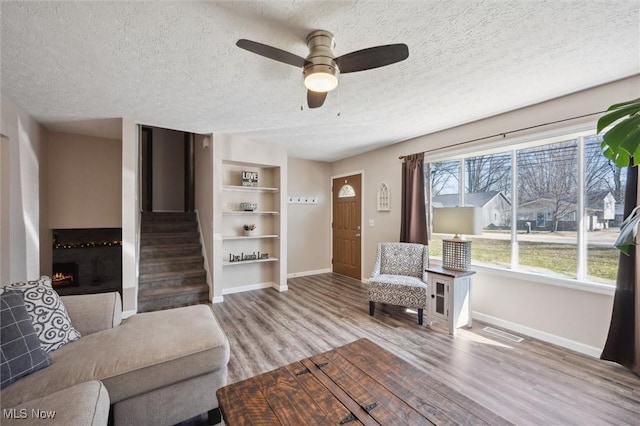 living area featuring wood finished floors, baseboards, stairs, a textured ceiling, and a large fireplace