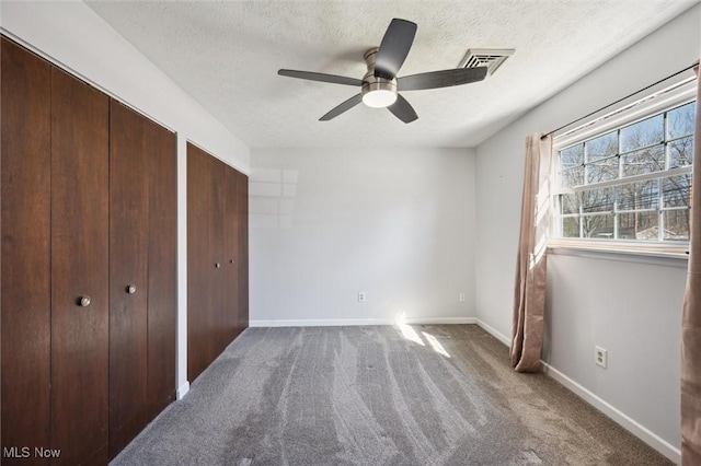 unfurnished bedroom featuring baseboards, a textured ceiling, multiple closets, and carpet floors