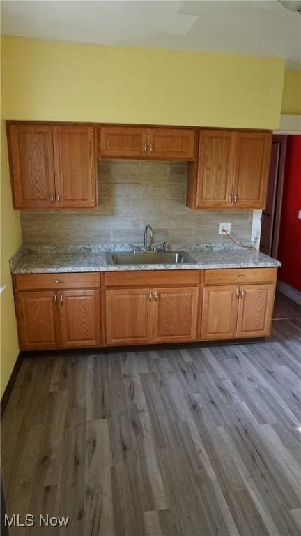 kitchen featuring backsplash, dark wood-type flooring, brown cabinets, and a sink