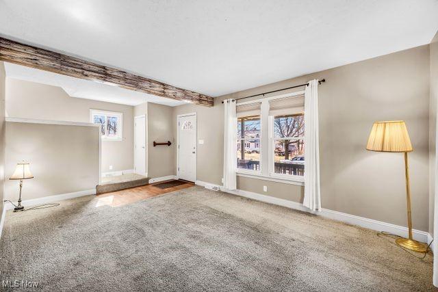 unfurnished living room featuring baseboards, carpet, and beam ceiling