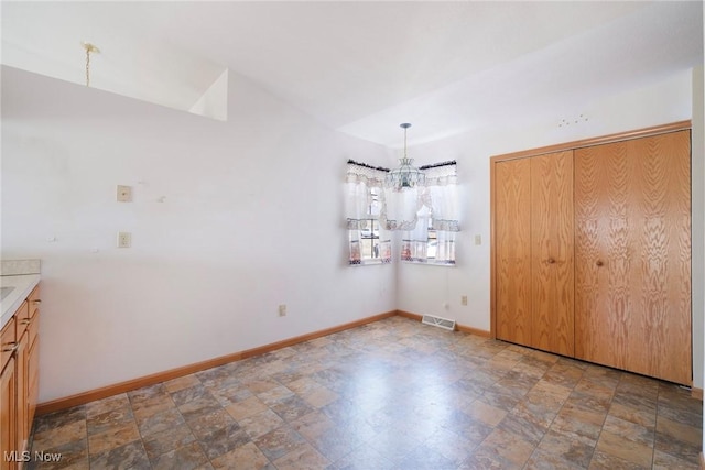 unfurnished dining area with stone finish flooring, visible vents, baseboards, and a chandelier