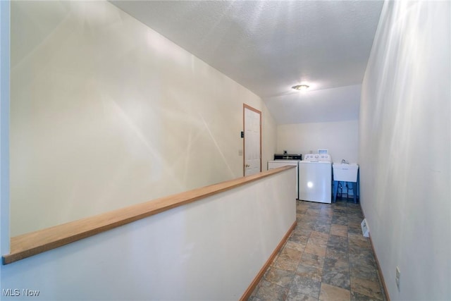 corridor featuring baseboards, washing machine and clothes dryer, a sink, vaulted ceiling, and stone finish flooring