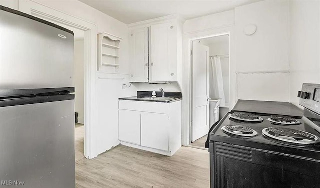 kitchen featuring dark countertops, light wood-type flooring, freestanding refrigerator, black electric range oven, and white cabinetry